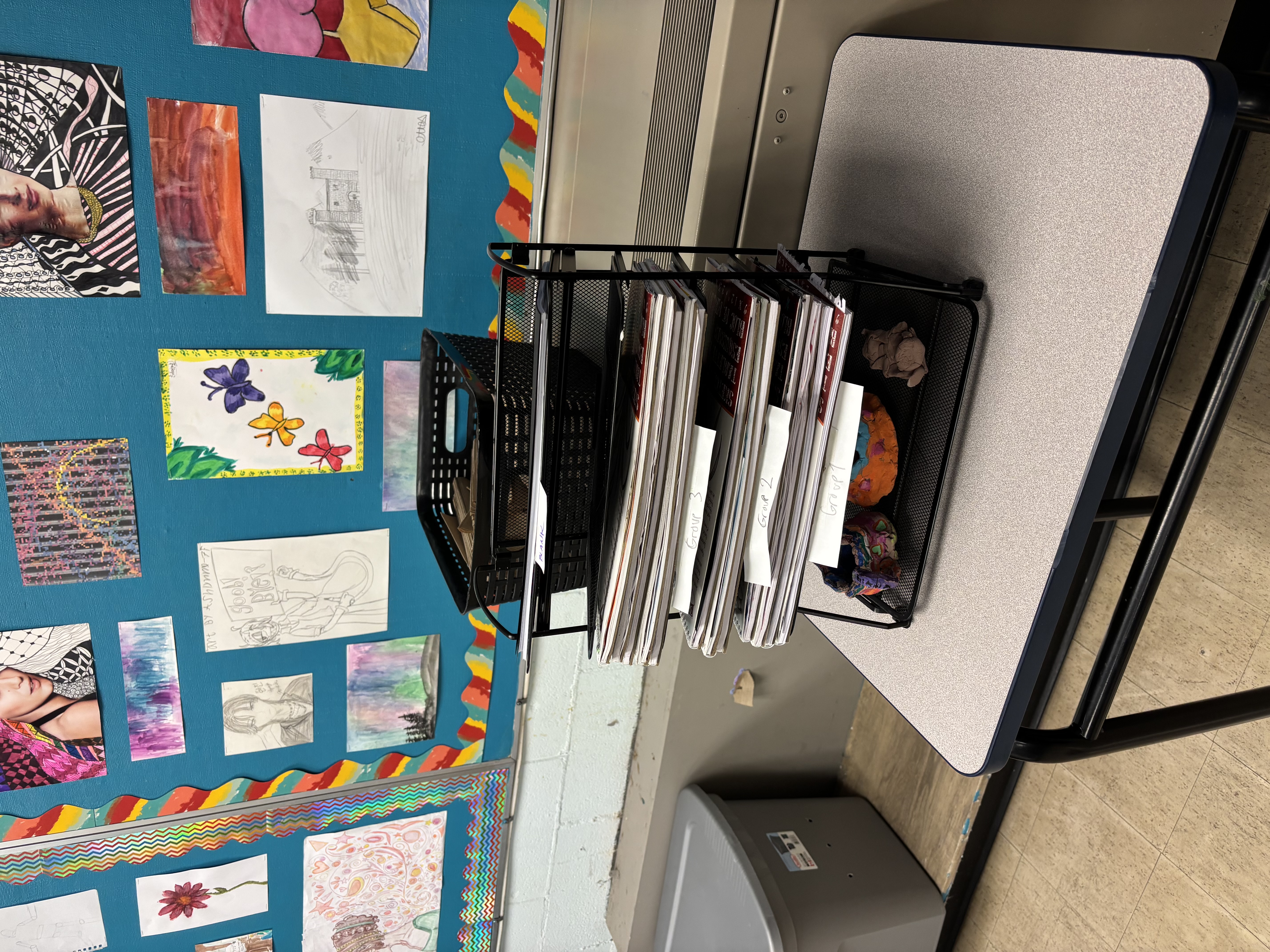 Student artwork displayed on a colourful bulletin board alongside organised portfolio folders